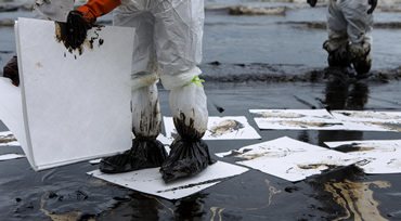 Crew in protective suits using absorbent pads at an oil spill