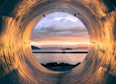 Large water pipe opening onto a calm bay at sunset